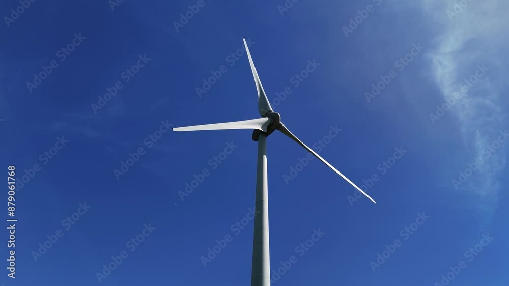Low Angle Spinning wind turbine, generating electricity. Summer time blue sky with few clouds. Low Angle Spinning wind turbine, generating electricity. Summer time blue sky with few clouds.