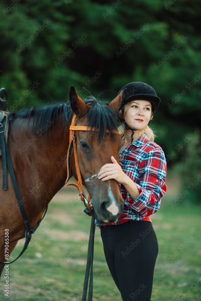 Obraz premium Happy blonde with horse in forest. Woman and a horse walking through the field during the day. Dressed in a plaid shirt and black leggings.