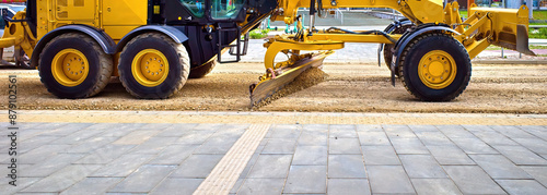 The grader levels the road. The blade of a motor grader in the process of leveling the sandy base of the road. A grader works on road construction. photo