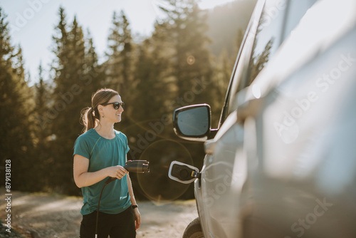 Smiling woman prepares to plug in and charge electric car photo