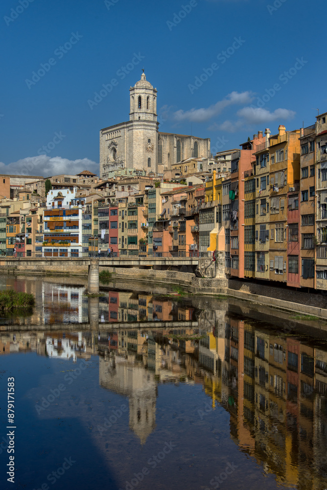 Obraz premium A view of the colourful buildings and Cathedral of Saint Mary of Girona reflected in the River Onya