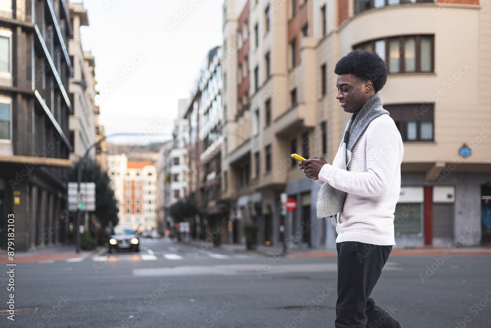 African young man walking in city street and using yellow mobile phone African young man walking in city street and using yellow mobile phone