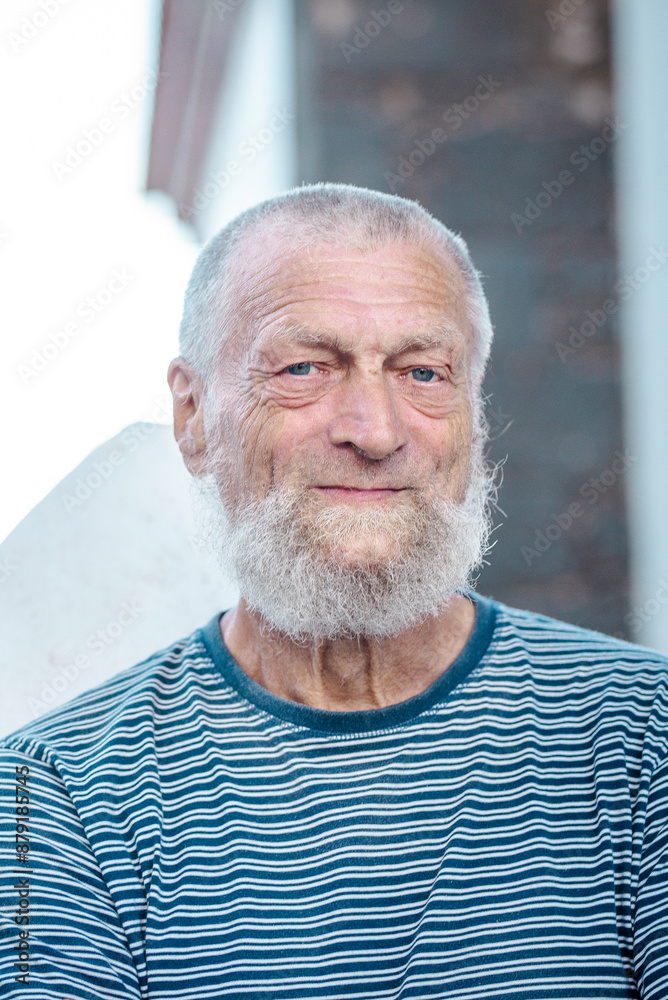 Portrait of standing mature old man looking on camera with serene expression and white beard and hair. Bright white house in background. Elderly people lifestyle. Tired face senior male outside Portrait of standing mature old man looking on camera with serene expression and white beard and hair. Bright white house in background. Elderly people lifestyle. Tired face senior male outside