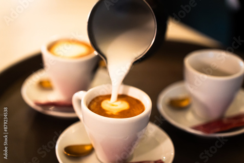 Stainless steel milk pitcher pouring into a coffee cup to make a cappuccino