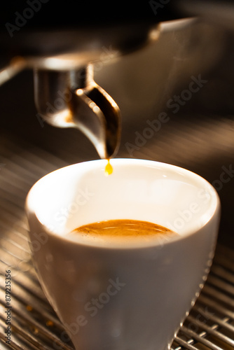 Close-up of an espresso cup filled with coffee in the machine. Vertical