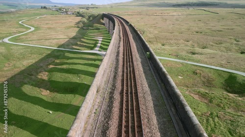 Curved railway track over viaduct bridge with long arch shadows at golden hour. Very close drone flyover following tracks. Ribblehead Viaduct, North Yorkshire, England, UK photo