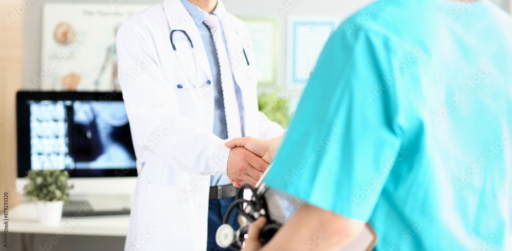 Two doctors in office shaking hands celebrating successful treatment closeup Two doctors in office shaking hands celebrating successful treatment closeup