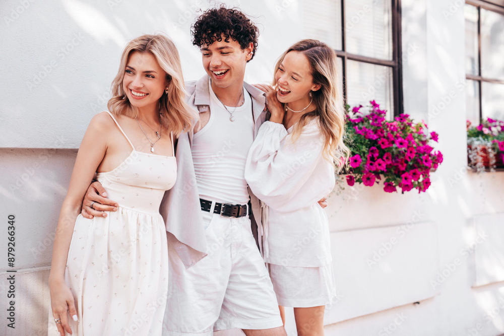 Young three stylish friends posing in the street. Fashion man and two cute female dressed in summer clothes. Smiling models having fun. Cheerful women and guy outdoors, in sunny day, Europe, Santorini Young three stylish friends posing in the street. Fashion man and two cute female dressed in summer clothes. Smiling models having fun. Cheerful women and guy outdoors, in sunny day, Europe, Santorini