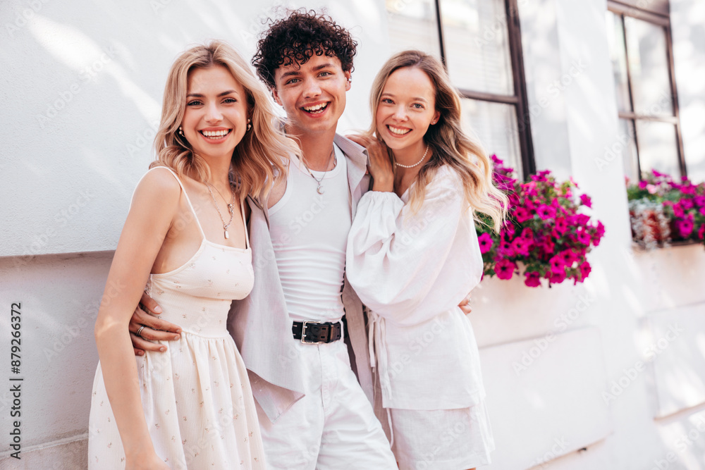 Young three stylish friends posing in the street. Fashion man and two cute female dressed in summer clothes. Smiling models having fun. Cheerful women and guy outdoors, in sunny day, Europe, Santorini Young three stylish friends posing in the street. Fashion man and two cute female dressed in summer clothes. Smiling models having fun. Cheerful women and guy outdoors, in sunny day, Europe, Santorini