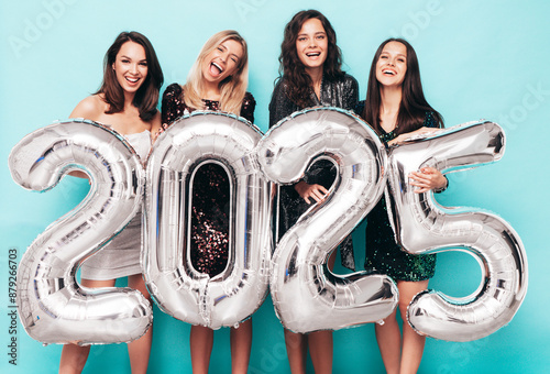 Four Beautiful women celebrating New Year. Happy gorgeous female in stylish sexy party dresses holding silver 2025 balloons, having fun at New Year's Eve Party. holiday celebration. Charming models photo