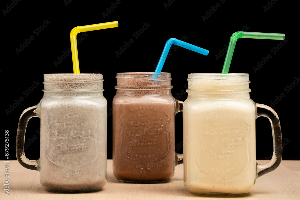 Three mason jar glasses filled with different smoothies and straws on a wooden table Three mason jar glasses filled with different smoothies and straws on a wooden table