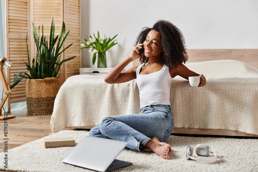 A curly African American woman in a tank top sitting on the floor, engaged in a phone conversation in a modern bedroom. A curly African American woman in a tank top sitting on the floor, engaged in a phone conversation in a modern bedroom.