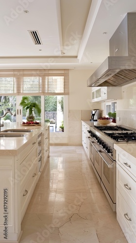 Modern white kitchen with stainless steel appliances, white cabinets, a black window frame, and a view of trees and greenery. Light grey tiled floor