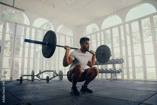 Young multiracial man in sportswear doing weightlifting exercises in squatting position at gym