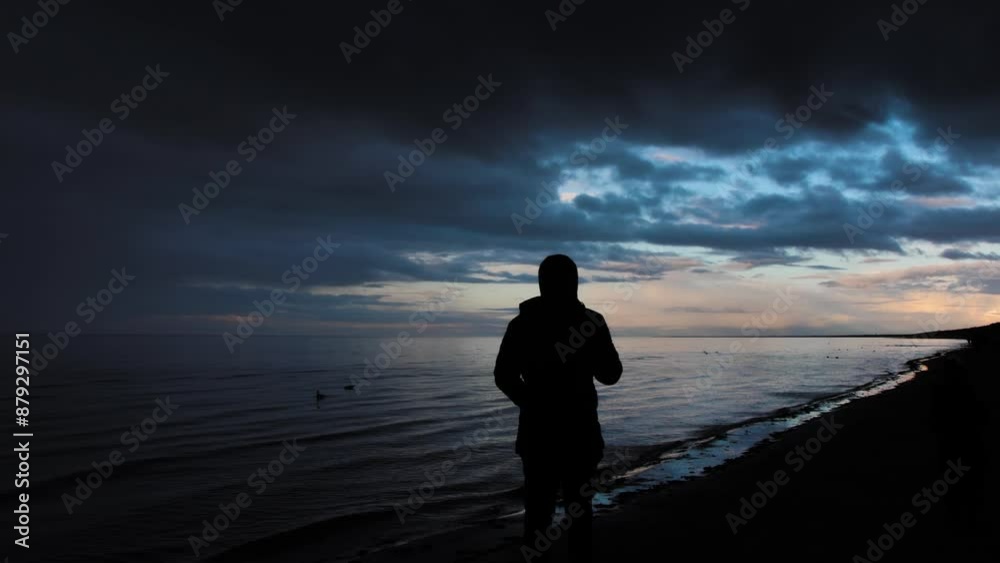 Contemplative persons silhouette by the calm shore at twilight, under a dramatic evening sky Contemplative persons silhouette by the calm shore at twilight, under a dramatic evening sky