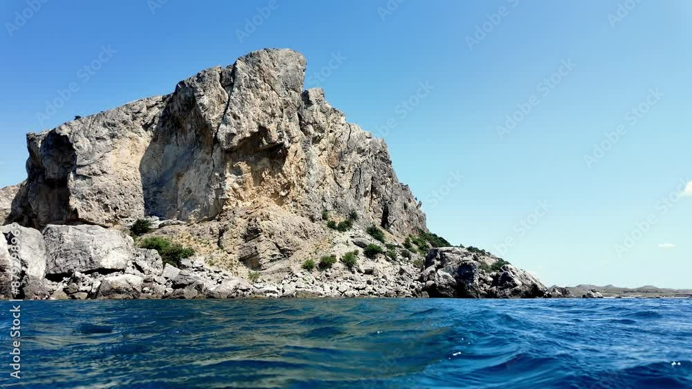 A view of the coastline near Sudak, Crimea, Russia. The clear blue waters of the Black Sea lap against the rocky shoreline. A view of the coastline near Sudak, Crimea, Russia. The clear blue waters of the Black Sea lap against the rocky shoreline.