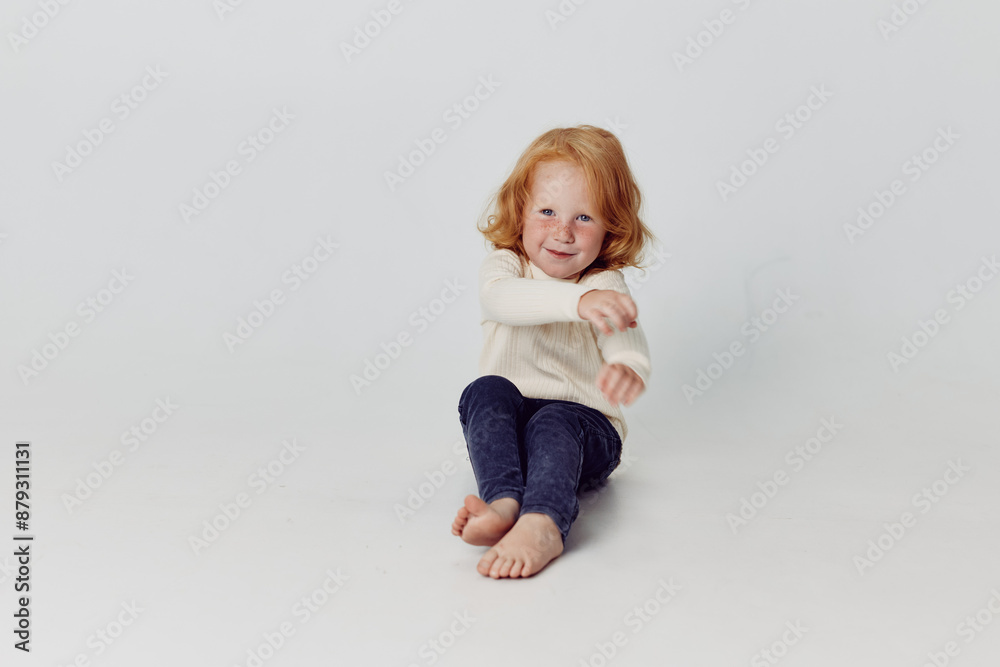 Happy little girl sitting on the floor with hands in the air in a white background for fashion and beauty concept Happy little girl sitting on the floor with hands in the air in a white background for fashion and beauty concept