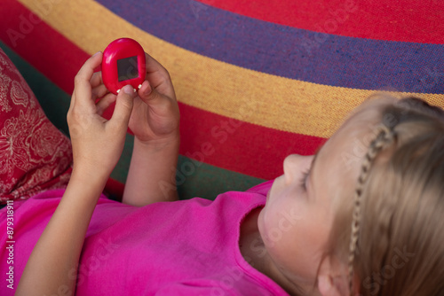 Little girl playing Tamagotchi toy while lying on a striped hammock. Popular game, caring for a virtual pet in the 90s. photo
