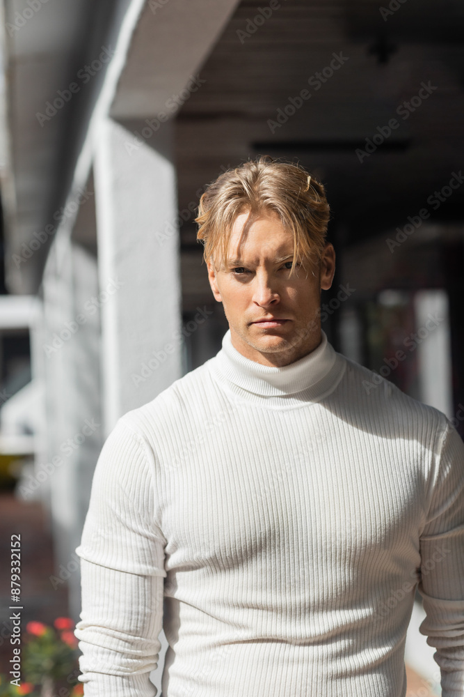 A blonde man poses in a white turtleneck sweater on a street in Florida. A blonde man poses in a white turtleneck sweater on a street in Florida.
