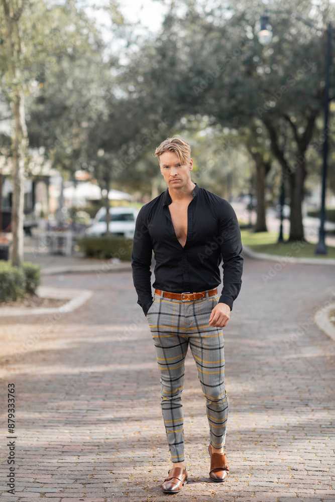 A handsome blonde man in a black shirt and plaid pants walks down a street in Orlando, Florida. A handsome blonde man in a black shirt and plaid pants walks down a street in Orlando, Florida.
