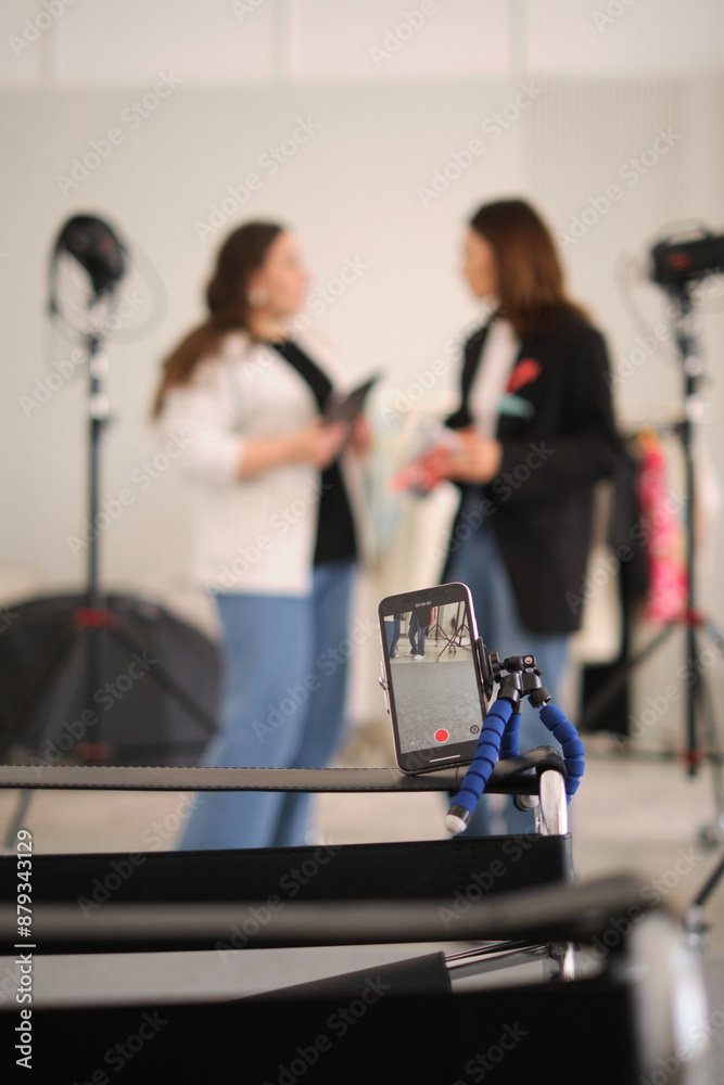 Two fashion bloggers are pictured in a studio, discussing new content ideas with a tablet and a magazine. The presence of lighting equipment suggests a photo or video shoot planning session. Two fashion bloggers are pictured in a studio, discussing new content ideas with a tablet and a magazine. The presence of lighting equipment suggests a photo or video shoot planning session.