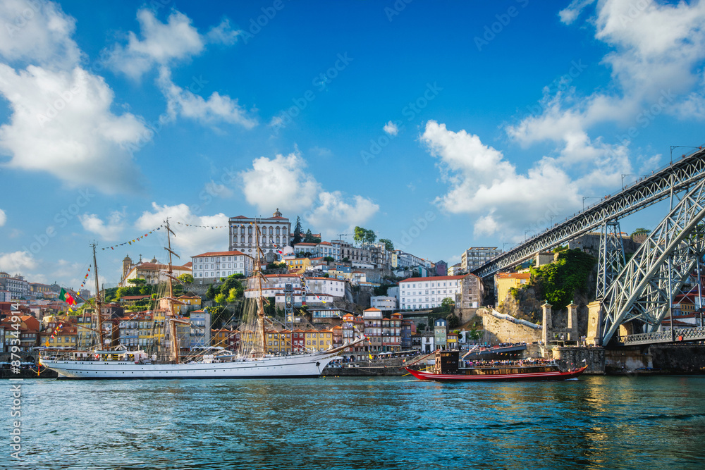 Naklejka premium View of Porto city and Douro river with traditional boats with port wine barrels and sailing ship from famous tourist viewpoint Marginal de Gaia riverfront. Porto, Vila Nova de Gaia, Portugal