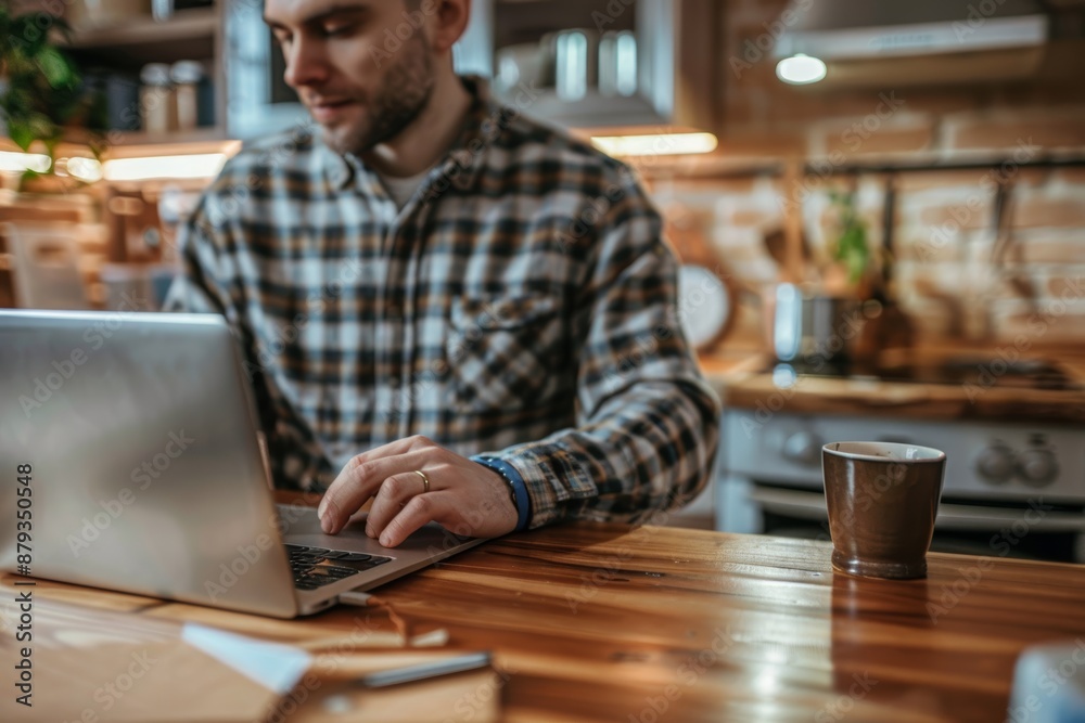 Young man working on a laptop from home, sitting in the kitchen while having a coffee Young man working on a laptop from home, sitting in the kitchen while having a coffee