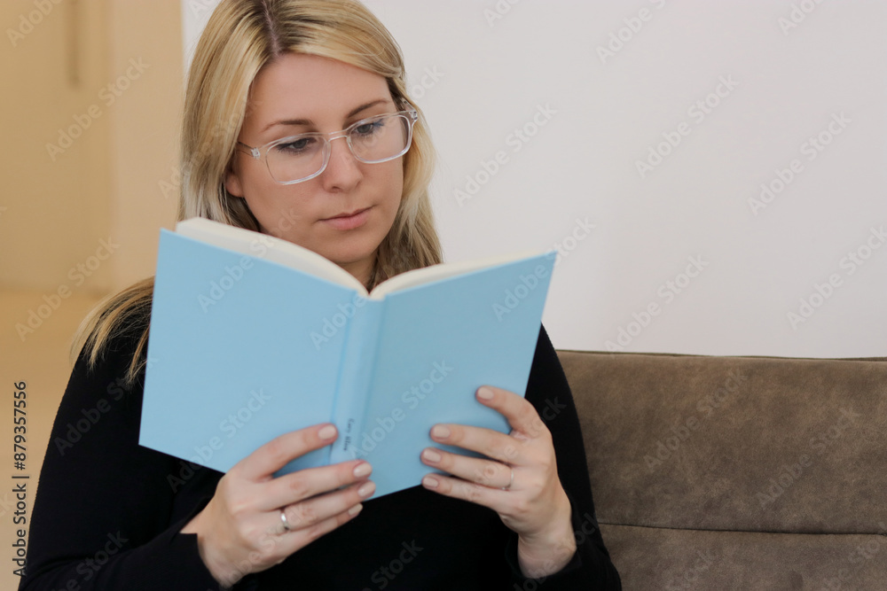 Close up portrait of a caucasian millennial female with glasses siting on a couch and reading a book Close up portrait of a caucasian millennial female with glasses siting on a couch and reading a book