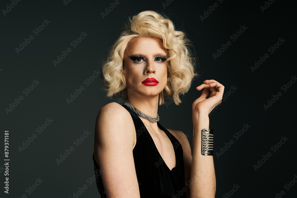 A drag queen with a blonde wig and dramatic makeup poses in a black dress against a dark background. A drag queen with a blonde wig and dramatic makeup poses in a black dress against a dark background.