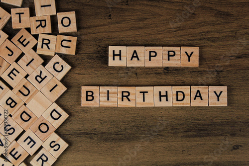 Photography Top view of square wooden tiles with the English alphabet scattered on a wooden background with happy birthday text