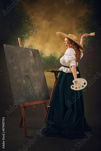 Emotional artist. Woman in historical attire, large straw hat, white blouse, and green velvet skirt, stands at easel painting with palette in hand, against vintage background. Comparison of eras photo