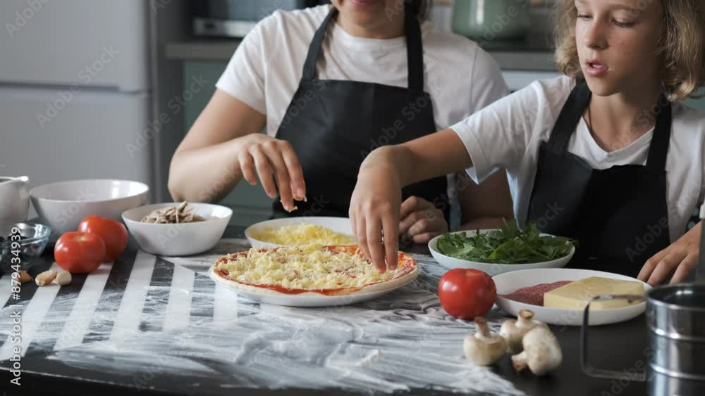 Mother and daughter sprinkle grated cheese on a homemade pepperoni pizza crust in their kitchen, enjoying the cooking process together Mother and daughter sprinkle grated cheese on a homemade pepperoni pizza crust in their kitchen, enjoying the cooking process together