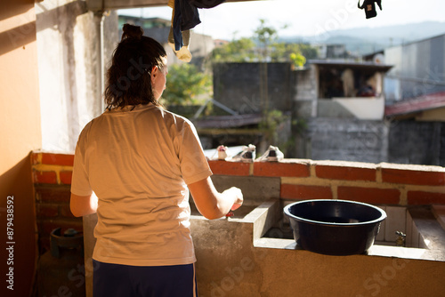 Woman washing clothes looking out window at favela