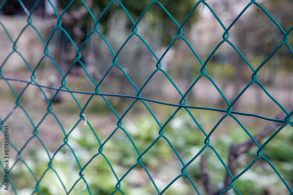 Fototapeta premium Close-up of a green wire mesh fence with a blurred garden in the background