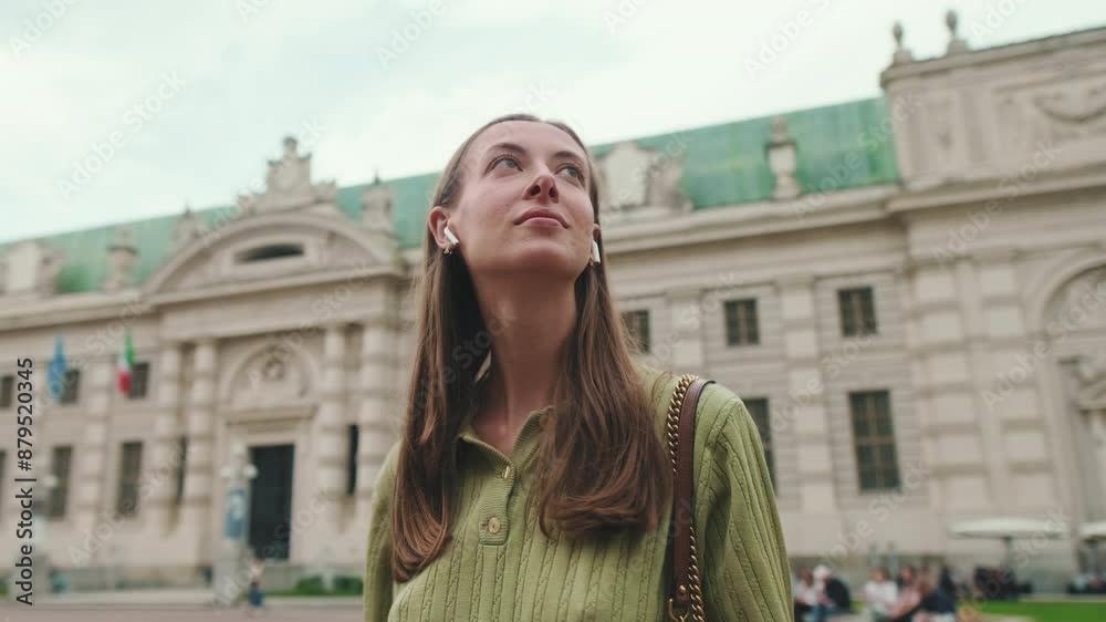 Young woman in wireless earphone looks around at old city background Young woman in wireless earphone looks around at old city background