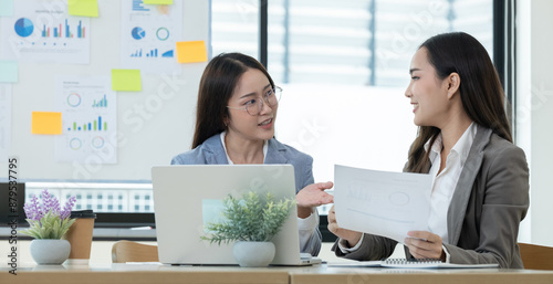 Two Female Accountant Collaborating on Financial Report in a Modern Office Setting with Laptop and Documents