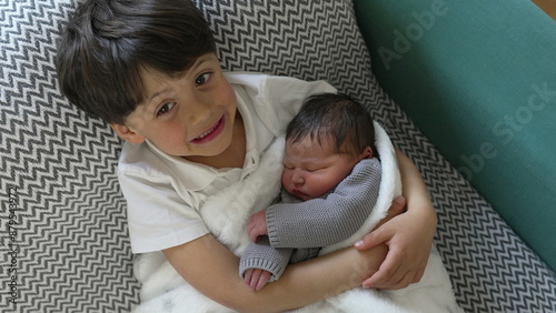 Young boy with a joyful expression holds his newborn sibling wrapped in a cozy blanket, showcasing a moment of pure happiness and brotherly love
