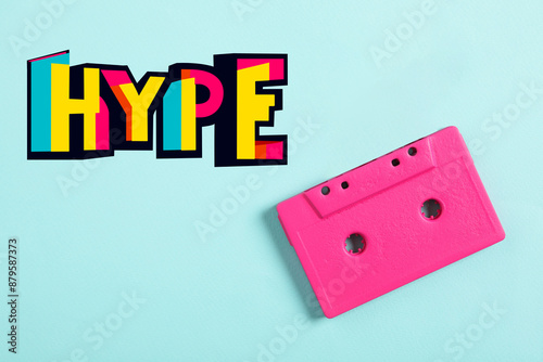 Fotografía Hype word of bright letters and pink audio cassette on cyan background, top view