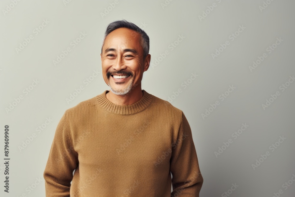 Portrait of a happy asian man in his 50s wearing a cozy sweater while standing against minimalist or empty room background Portrait of a happy asian man in his 50s wearing a cozy sweater while standing against minimalist or empty room background