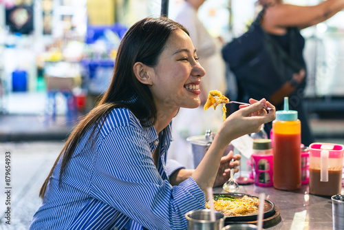 Young Asian woman traveler tourist eating Thai street food in China town night market in Bangkok in Thailand - people traveling enjoying food culture concept