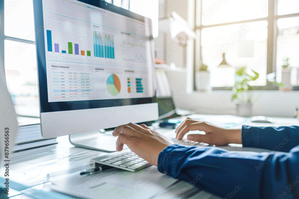 Person analyzing business data on a computer screen, displaying charts and graphs, in a bright office setting. Person analyzing business data on a computer screen, displaying charts and graphs, in a bright office setting.