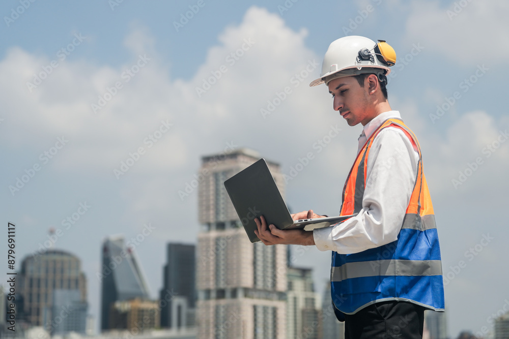 A male engineer works with communications on the roof of a tall building with surrounding engineering systems.