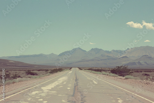 Retro vibe image of an empty asphalt road through a desert landscape with mountains in the distance