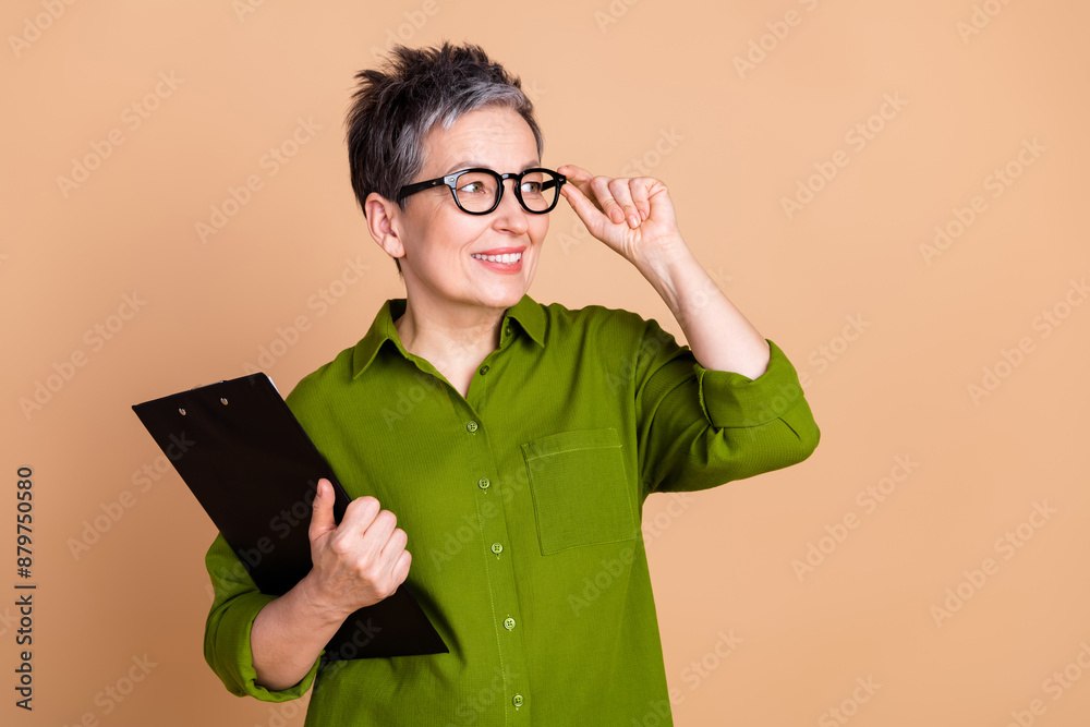 Photo portrait of pretty senior female look empty space documents wear trendy green outfit isolated on beige color background Photo portrait of pretty senior female look empty space documents wear trendy green outfit isolated on beige color background