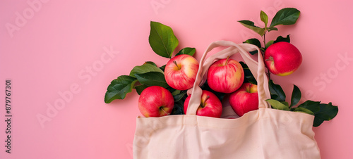 A canvas tote bag filled with apples on a pink background photo