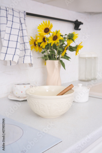 Home kitchen summer interior - Bowl with dough, bowl of sugar, cup of tea, ceramic vaze with flowers on kitchen table in modern kitchen.