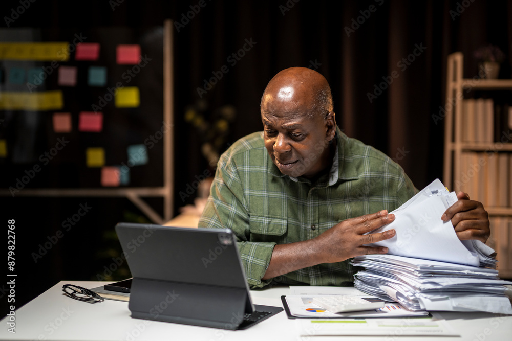 A man is sitting at a desk with a laptop and a stack of papers A man is sitting at a desk with a laptop and a stack of papers