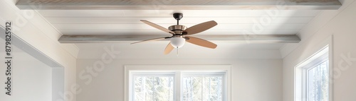 Modern ceiling fan with wooden blades in a bright, minimalist room with white walls and large windows for natural light.
