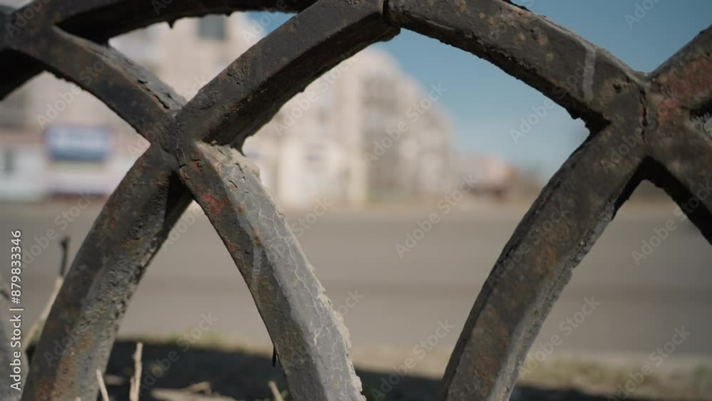 Close view of a weathered metal fence with intricate patterns,with cars passing by the road with a blur view of a city building Close view of a weathered metal fence with intricate patterns,with cars passing by the road with a blur view of a city building