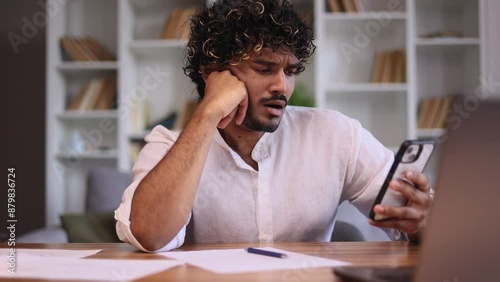 Boring young indian man scrolling feed of social networks products in internet store on smartphone while take a break indoors Tired exhausted female look at screen without enthusiasm at home workplace